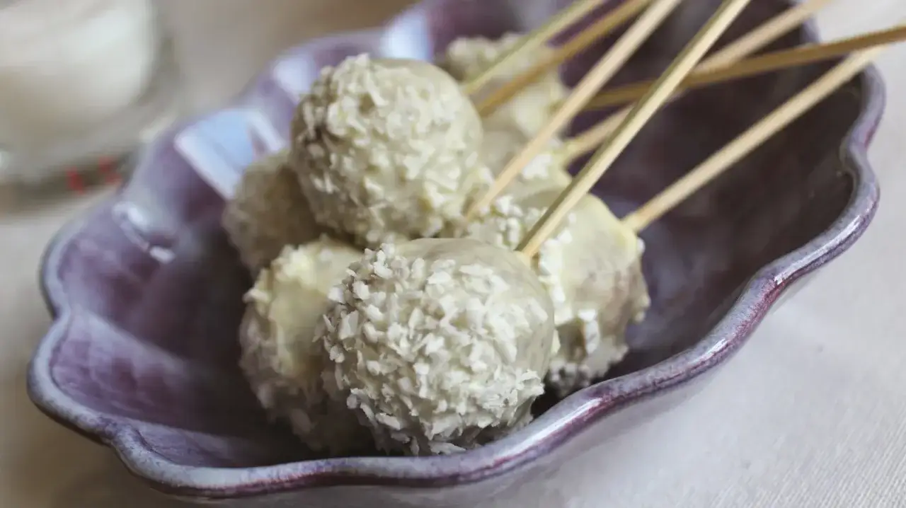 Söta cake pops pepparkaka, doppade i vit choklad och kokosflingor, serveras i en lila skål.