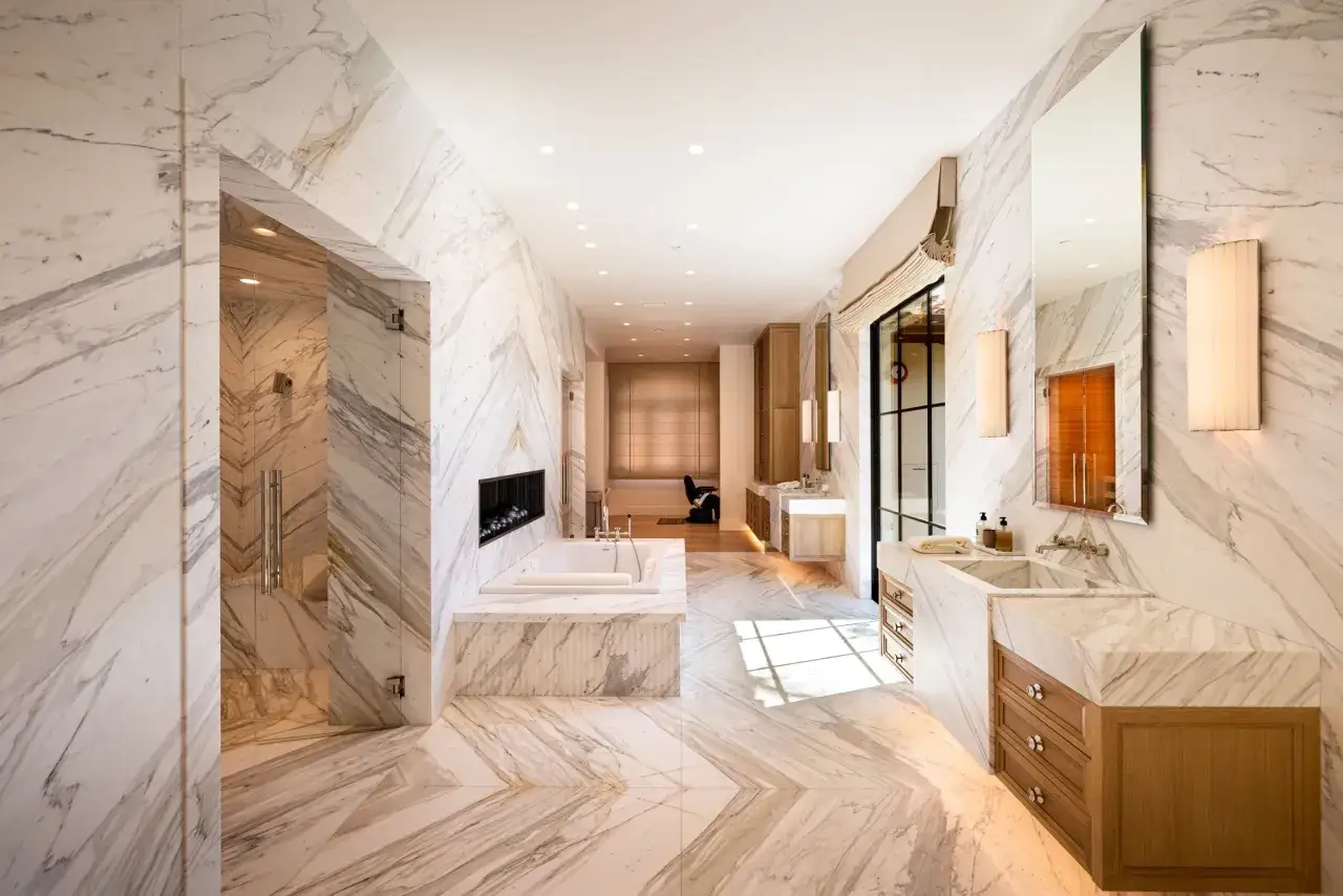 Bagno lussuoso con vasca, doccia e doppio lavabo, tutto rivestito in **scanalatura del marmo** con venature dorate.