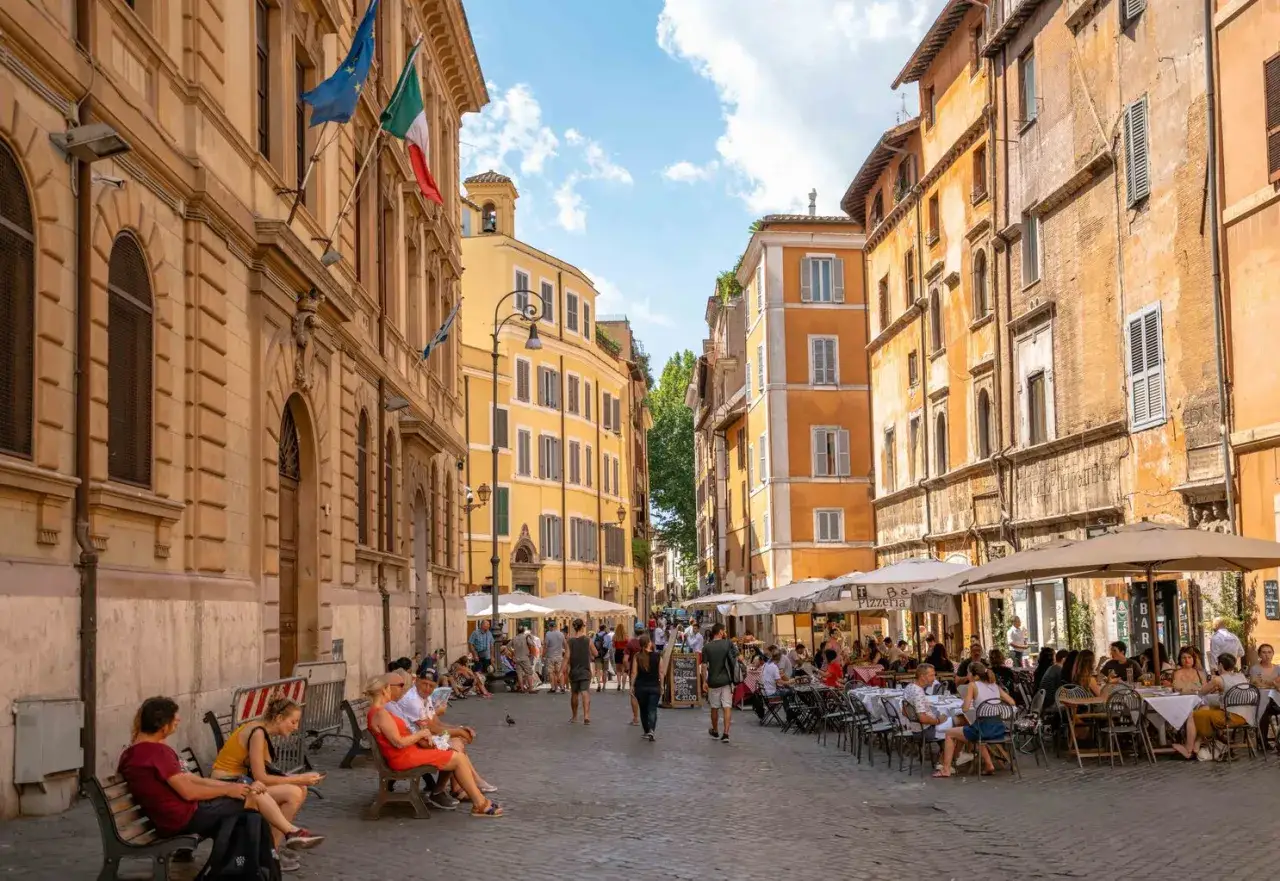 Una strada animata nel quartiere ebraico di Roma, con edifici storici, tavolini all'aperto di ristoranti e persone che passeggiano e si rilassano.