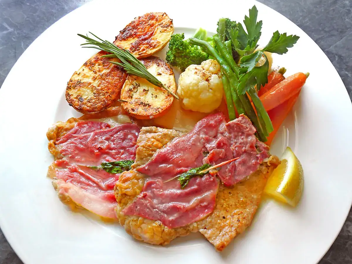Ein Teller mit Saltimbocca Rezept Original: Kalbsschnitzel mit Schinken und Salbei, dazu Bratkartoffeln und gemischtes Gemüse.