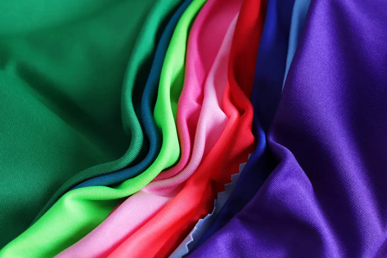 A vibrant collection of athletic wear fabric in various colors, including green, pink, red, blue, and purple, draped in soft folds.