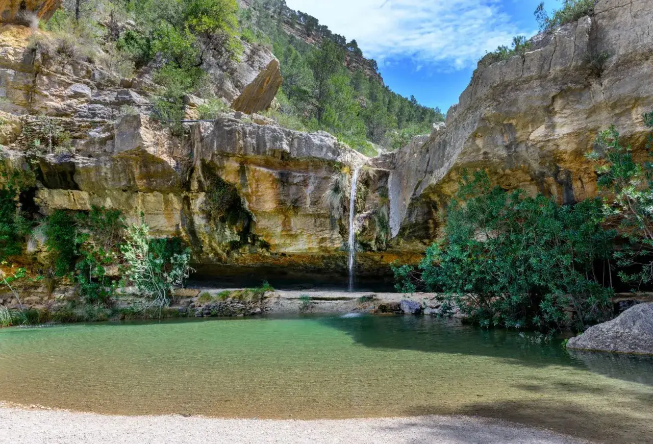 Cascada cayendo en un estanque de aguas cristalinas, rodeado de rocas y vegetación. Un lugar idílico para disfrutar de los charcos de quesa.