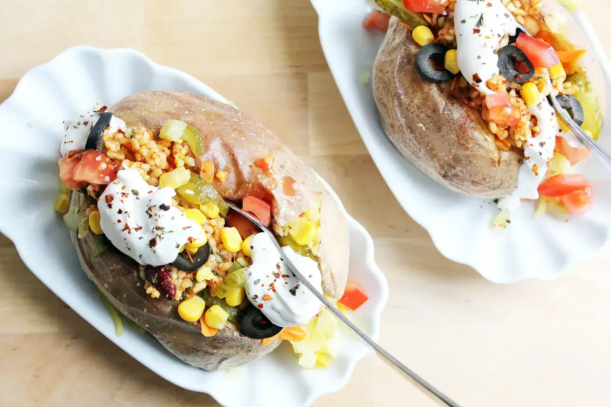 Zwei gefüllte Ofenkartoffeln, ein leckeres Kumpir Rezept, mit Reis, Mais, Oliven, Tomaten und einem Klecks Joghurt.