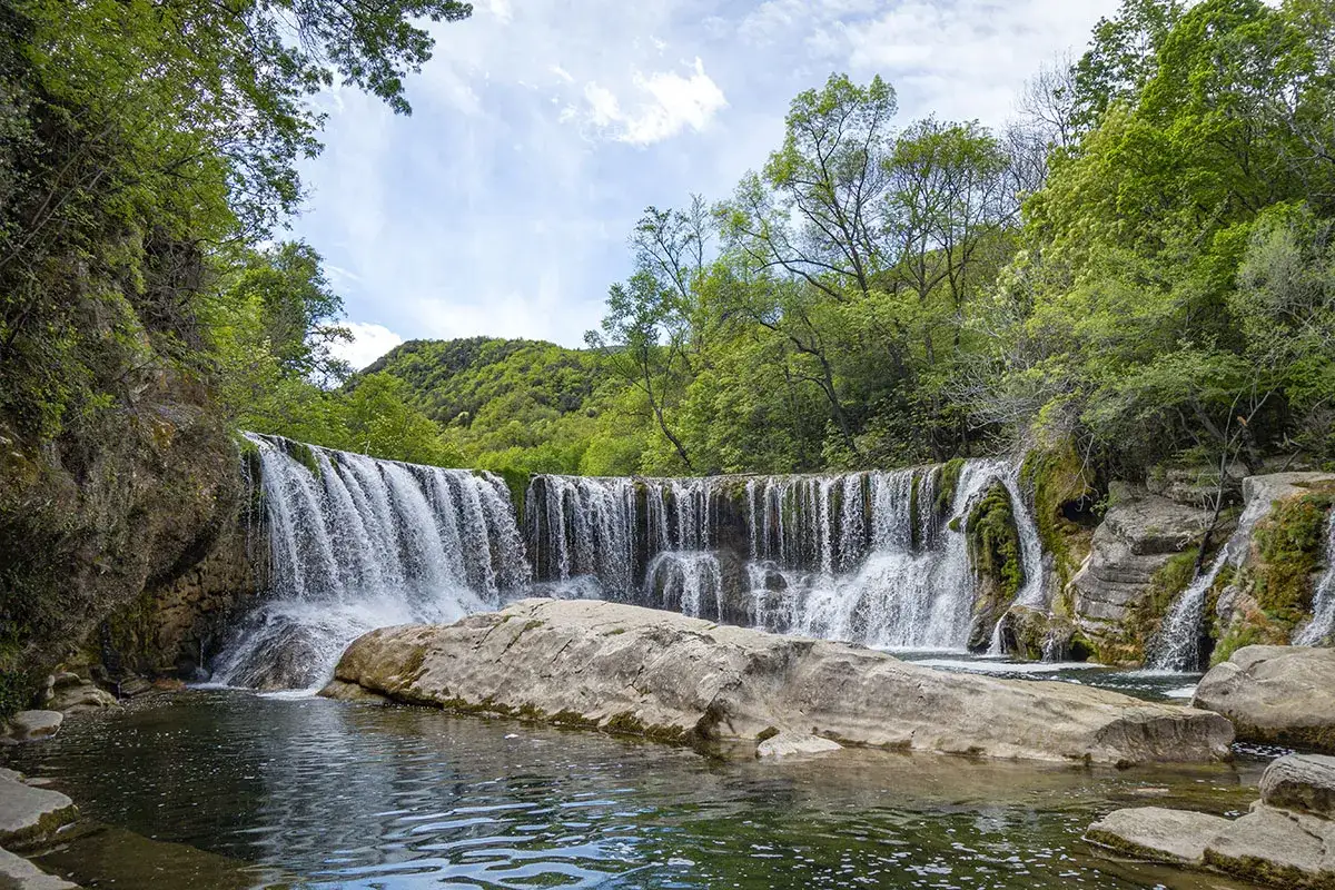 Cascade d'eau dans le cirque de Navacelles, entourée de verdure luxuriante et de rochers.