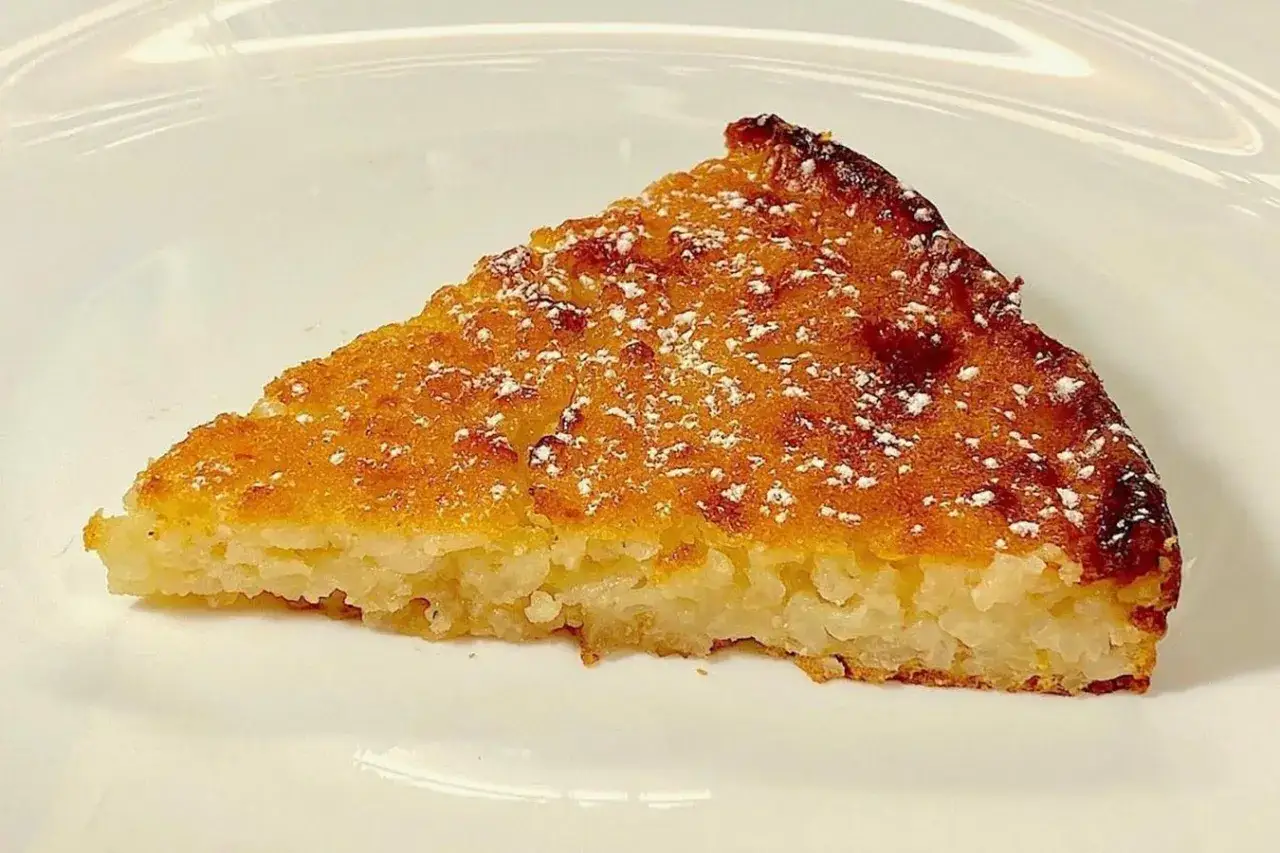 Una fetta di budino di riso cotto al forno, cosparso di zucchero a velo, su un piatto bianco.