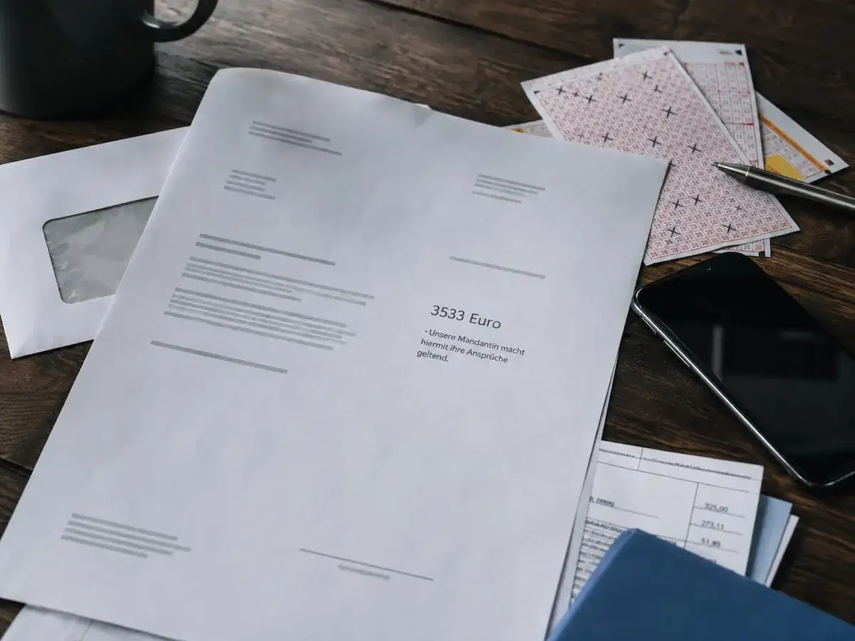 Papierkram, Lottoscheine und Handy auf Holztisch. Was tun, wenn angeblich Lotto-Abo abgeschlossen wurde?