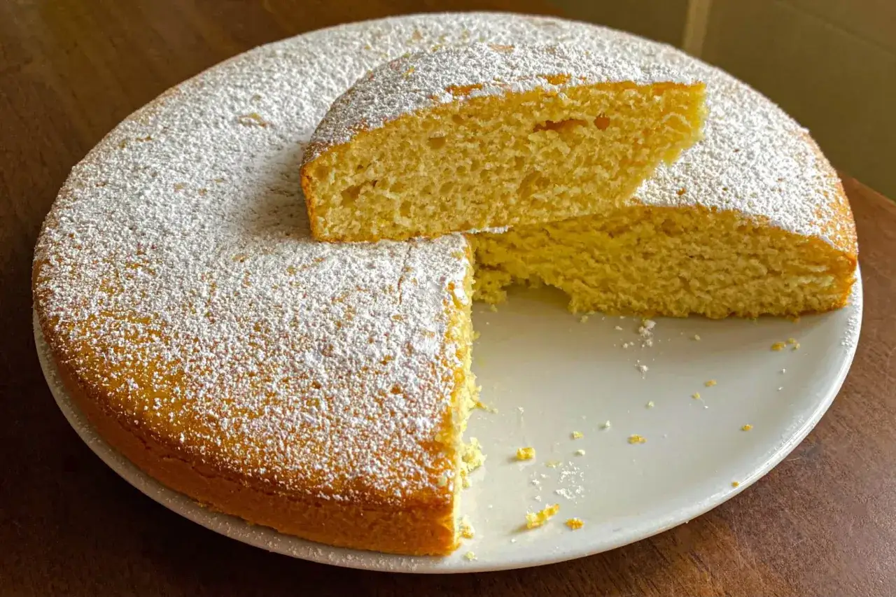 Un soffice plumcake al limone, cosparso di zucchero a velo, con una fetta tagliata che ne rivela la morbida consistenza.