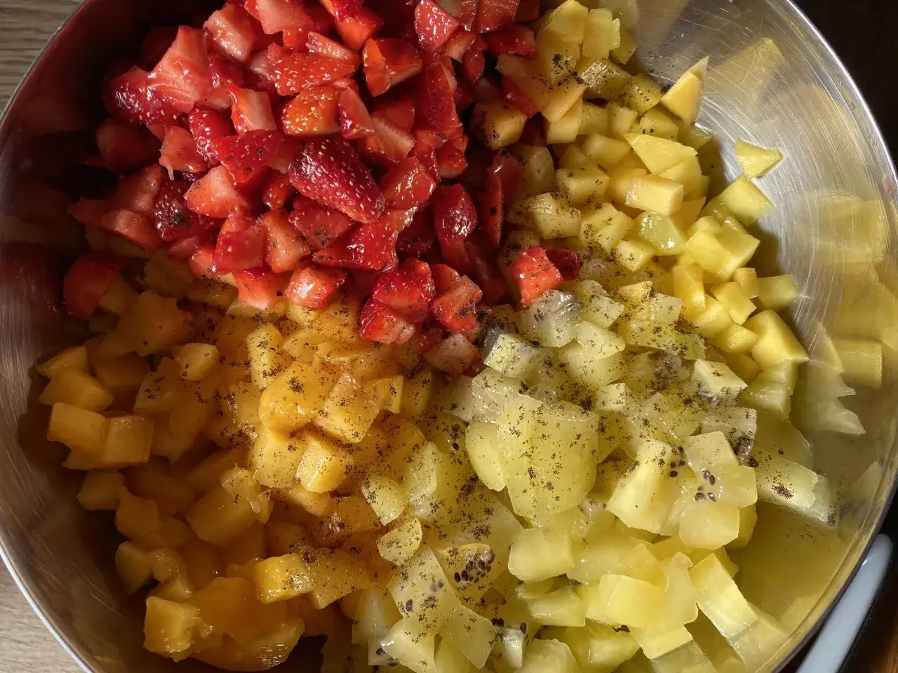 Un bol rempli de morceaux de fraises, de mangues et de kiwis, prêts à être mélangés pour une délicieuse salade de fruits.