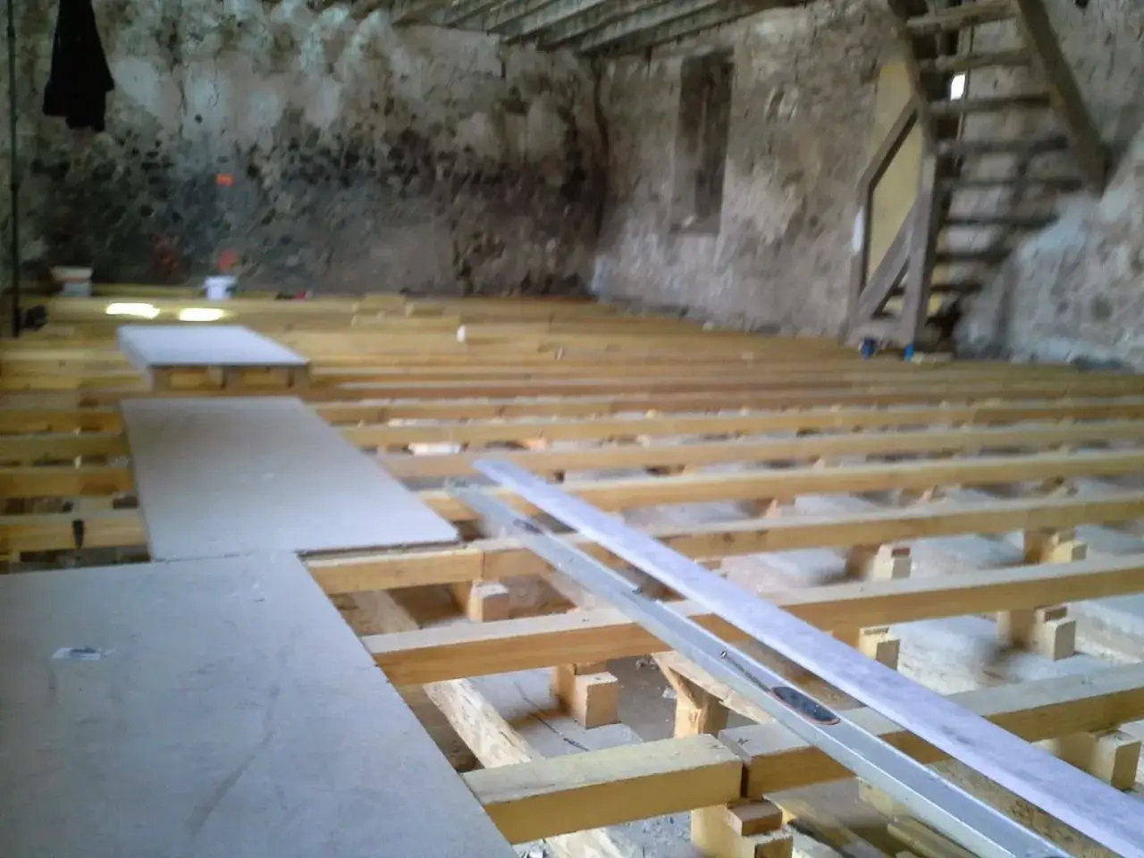 Pose de plancher OSB sur solives en bois dans une pièce en rénovation. Des panneaux sont déjà posés.