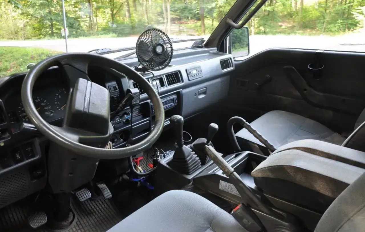 Wnętrze kampera Mitsubishi L300. Widok na deskę rozdzielczą, kierownicę, fotele i dźwignie bieg&oacute;w.