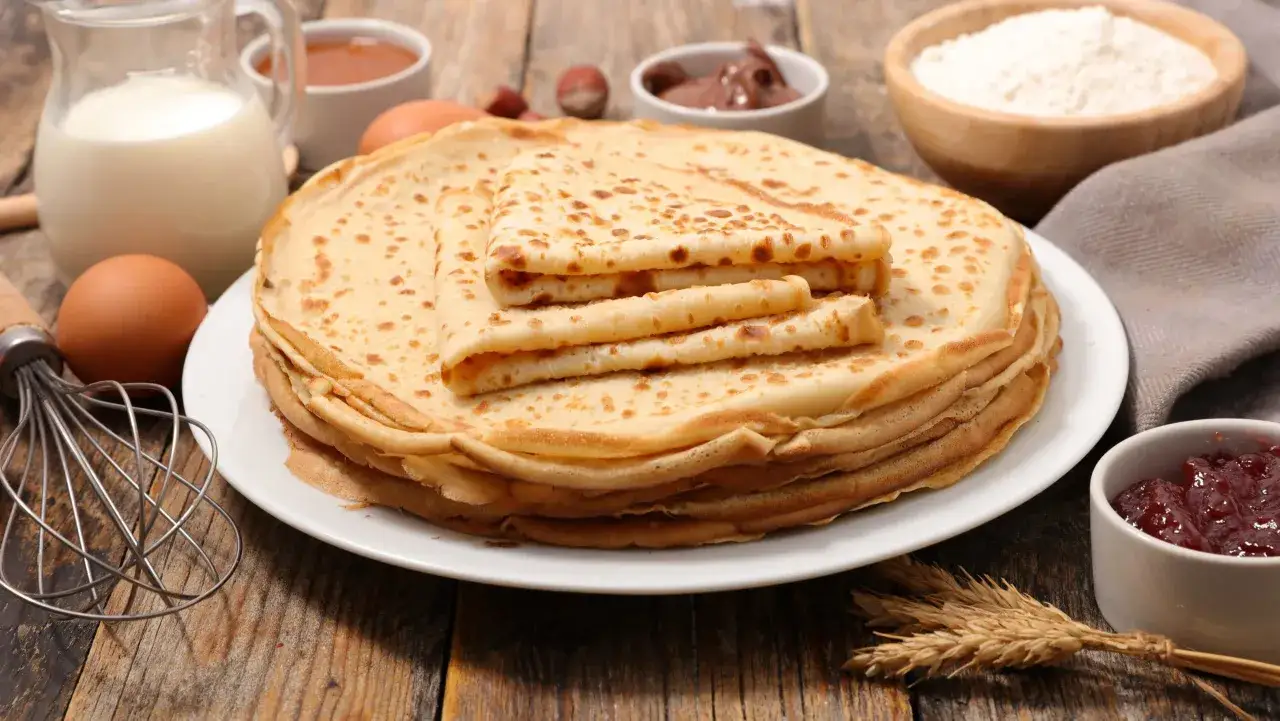 En h&ouml;g med nygr&auml;ddade pannkakor, redo att frysa in f&ouml;r senare. Ingredienser som mj&ouml;lk, &auml;gg och mj&ouml;l syns i bakgrunden.