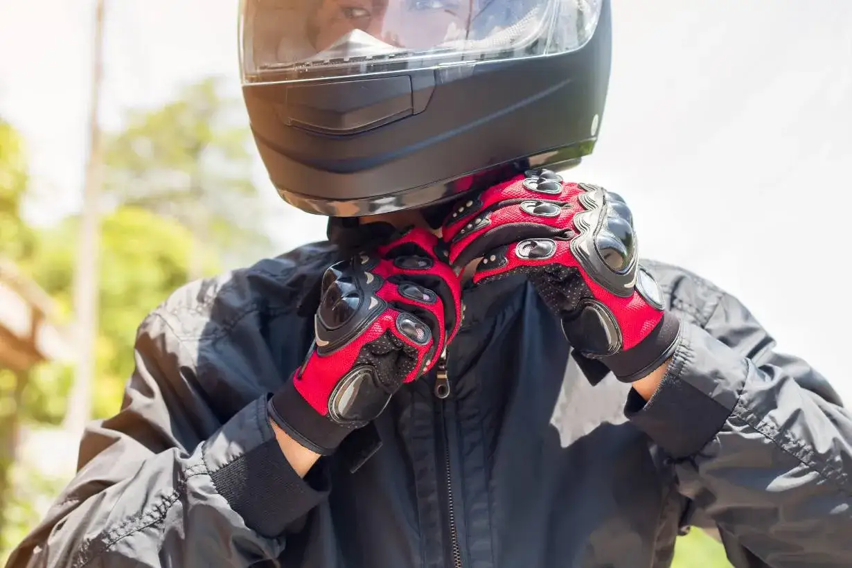 Motocyklista zapina rękawice z ochraniaczami, przygotowując się do jazdy. Różne rodzaje ochraniaczy zapewniają bezpieczeństwo.