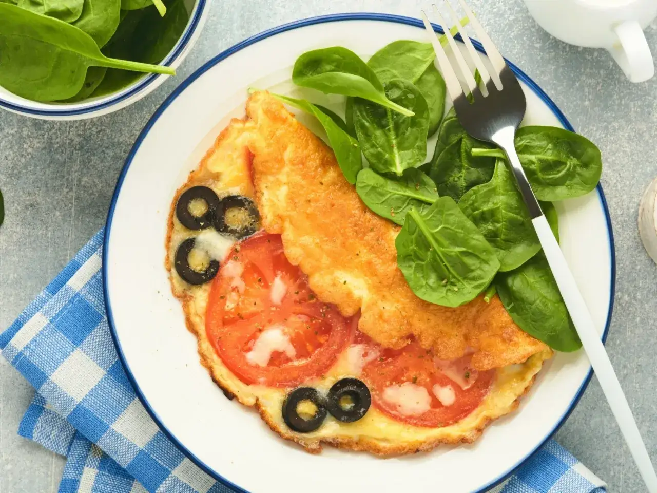 Pyszny omlet wytrawny z pomidorami i oliwkami, podany ze świeżym szpinakiem. Idealny na śniadanie lub lekki obiad.