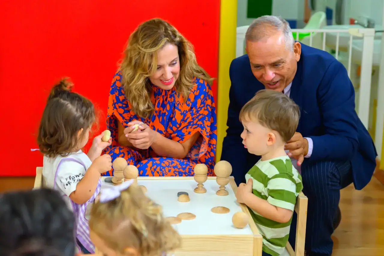 Adultos interactúan con niños pequeños en una mesa de juegos. La escena evoca la importancia del **ayuda bono infantil** para el desarrollo temprano.