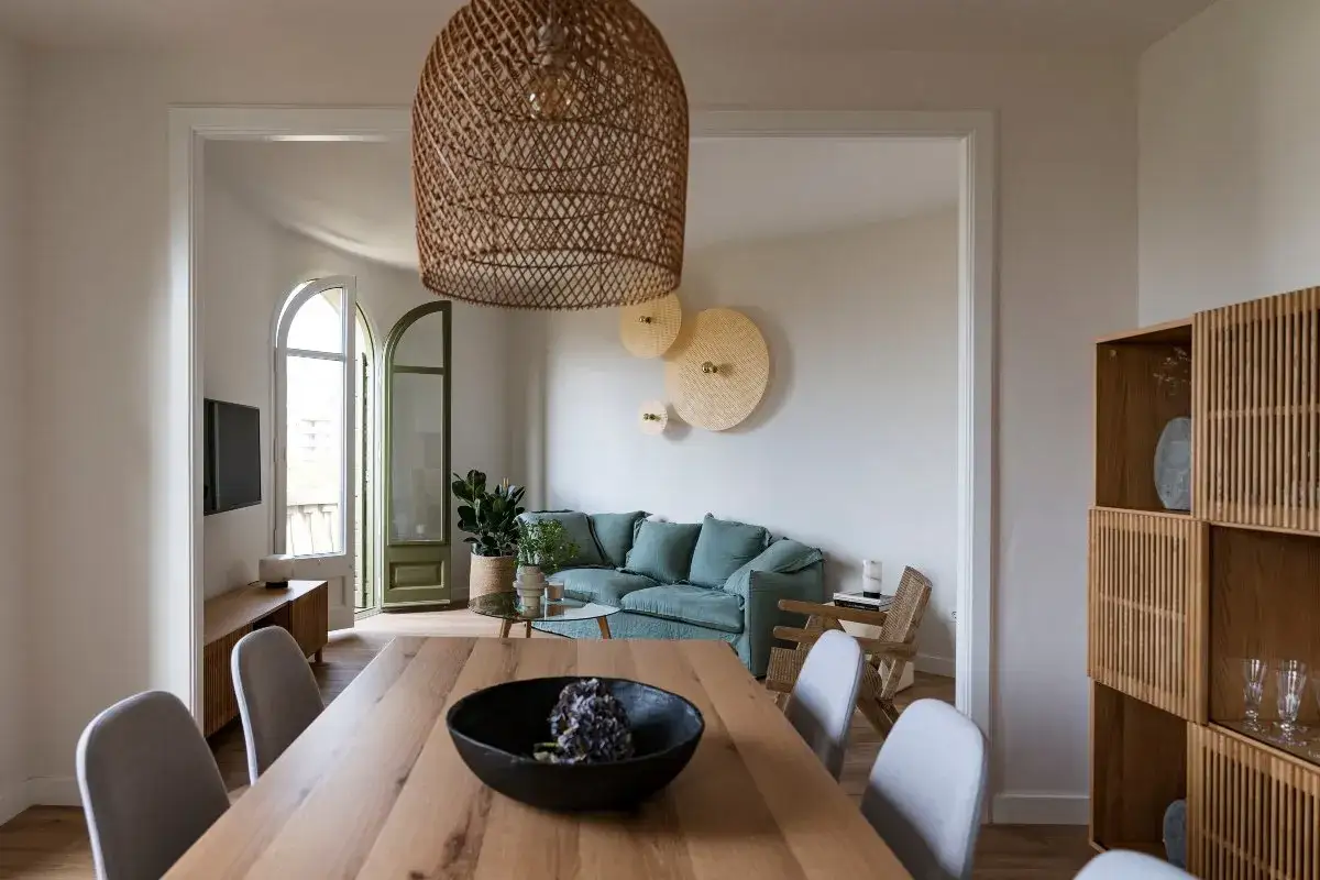 Comedor y sala minimalista para espacios peque&ntilde;os. Mesa de madera, sillas grises, sof&aacute; verde menta y gran l&aacute;mpara de mimbre.