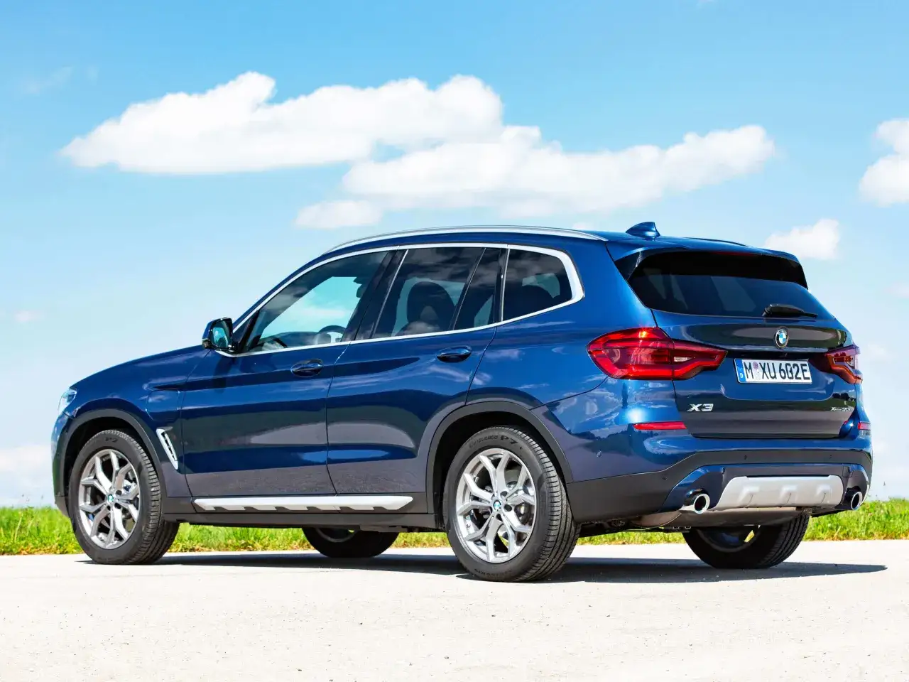 Błękitne BMW X3 z pięknymi felgami stoi na tle błękitnego nieba z chmurami. Zastanawiasz się, ile kosztuje BMW X3?