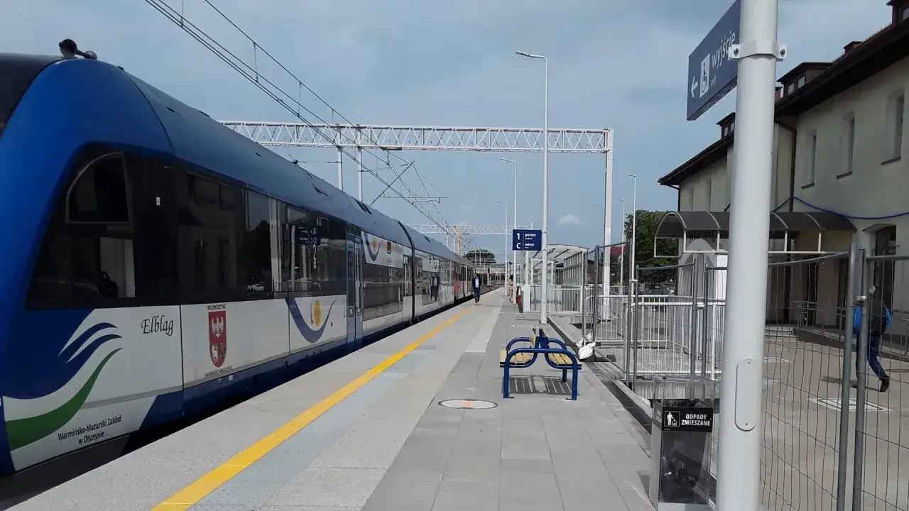 Pociąg do Giżycka stoi na peronie. W tle budynek dworca i niebo.
