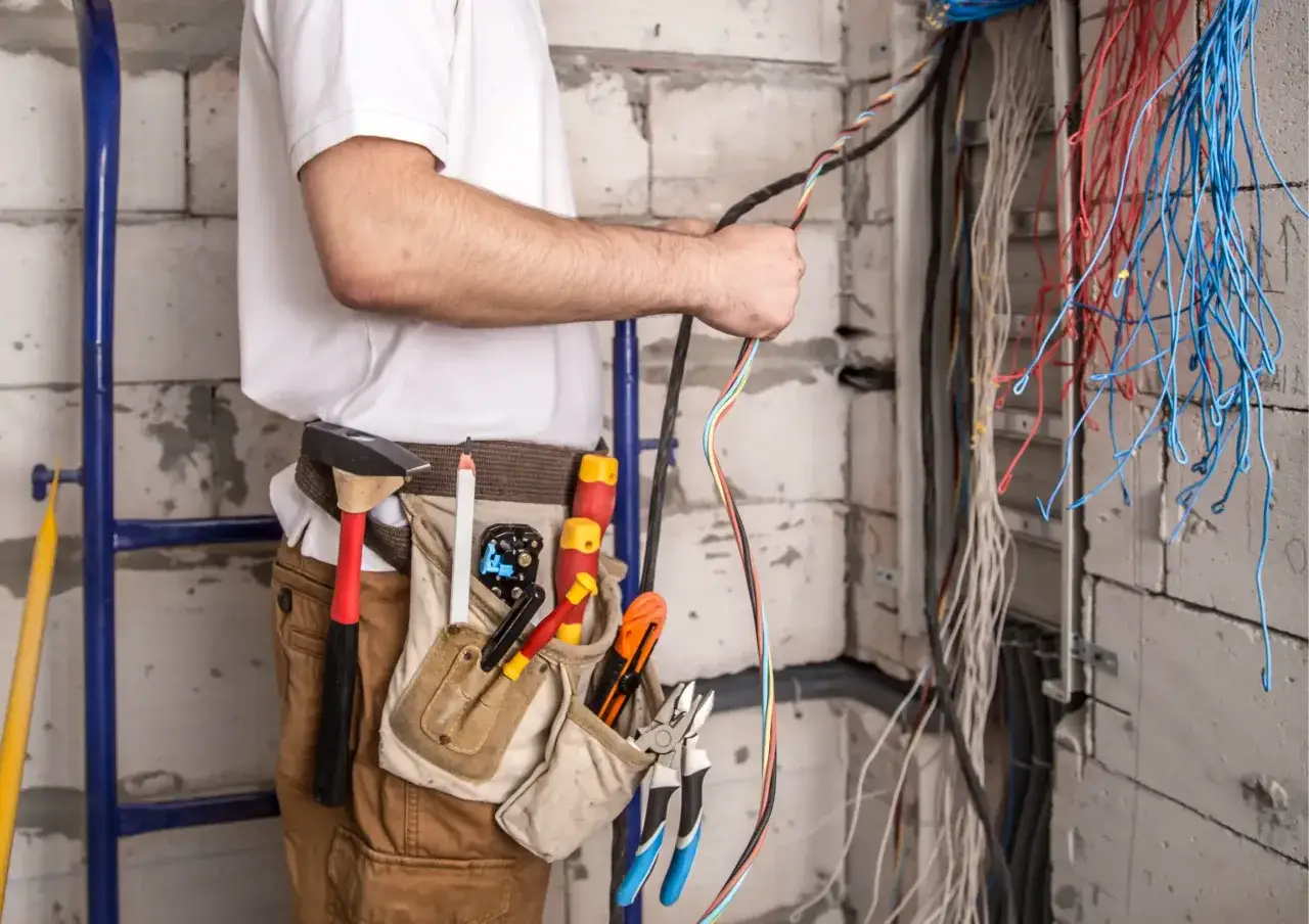 Elektryk z narzędziami przy pasie pracuje przy instalacji elektrycznej. Widać wiązki przewodów, a także narzędzia, które mogą być używane do montażu przekładników prądowych.