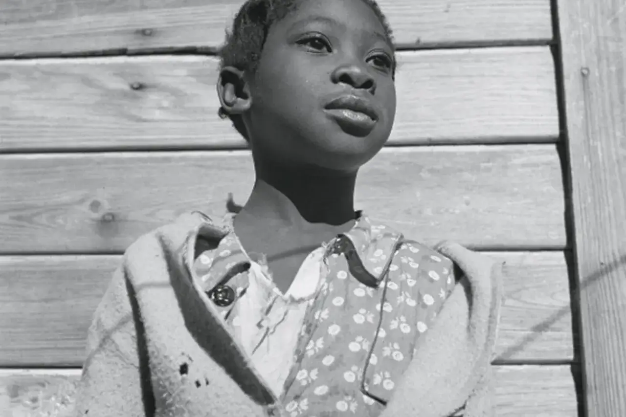 Dziecko patrzy w dal, w tle drewniana ściana. Ikoniczne ujęcie Gordona Parks'a.