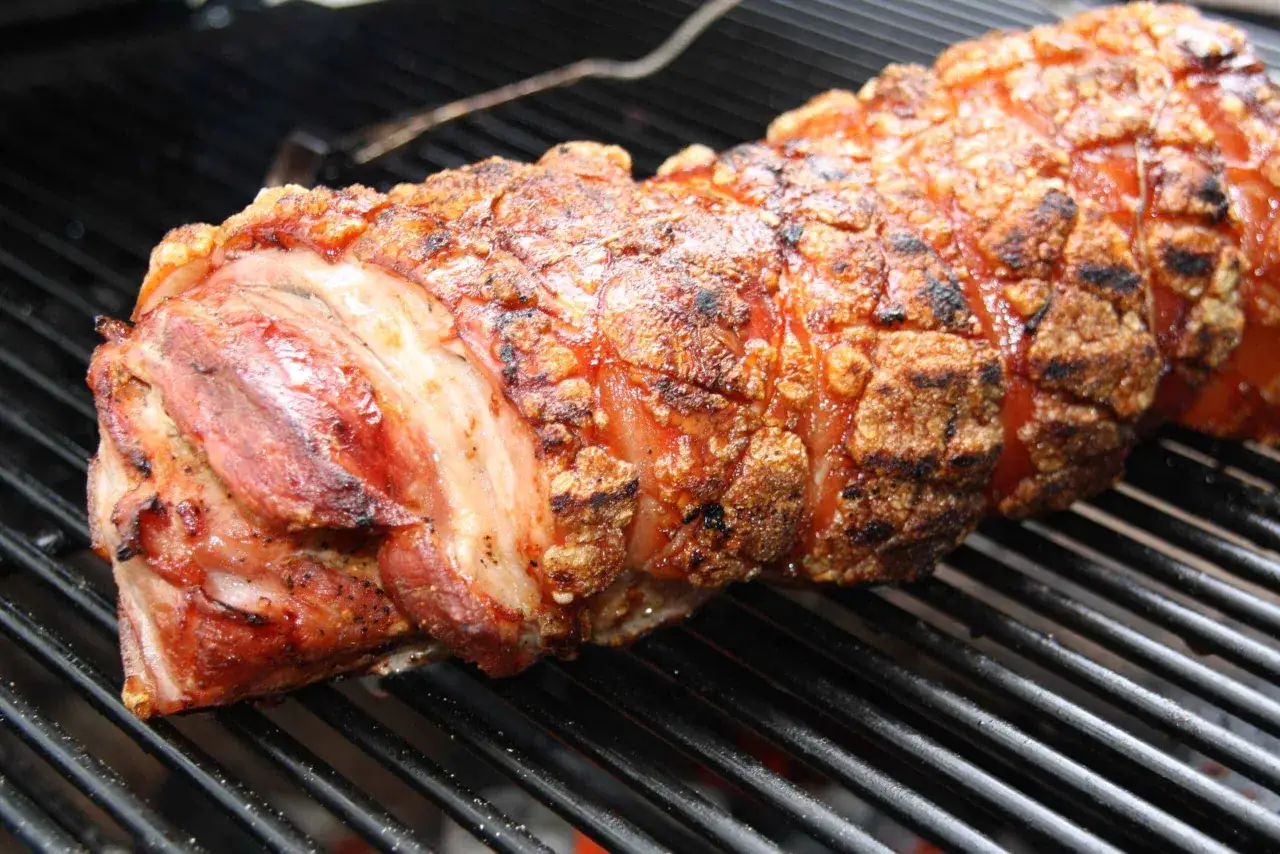 Ein knuspriges Spanferkel wird auf dem Grill zubereitet. Die Schwarte ist goldbraun und karamellisiert, während das Fleisch saftig aussieht.