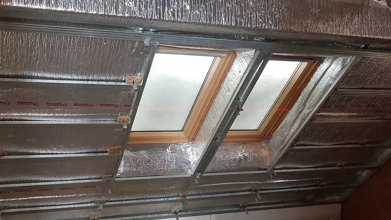 Ocieplenie poddasza w trakcie prac. Widoczne okna dachowe, profile metalowe i materiał izolacyjny z folią aluminiową.