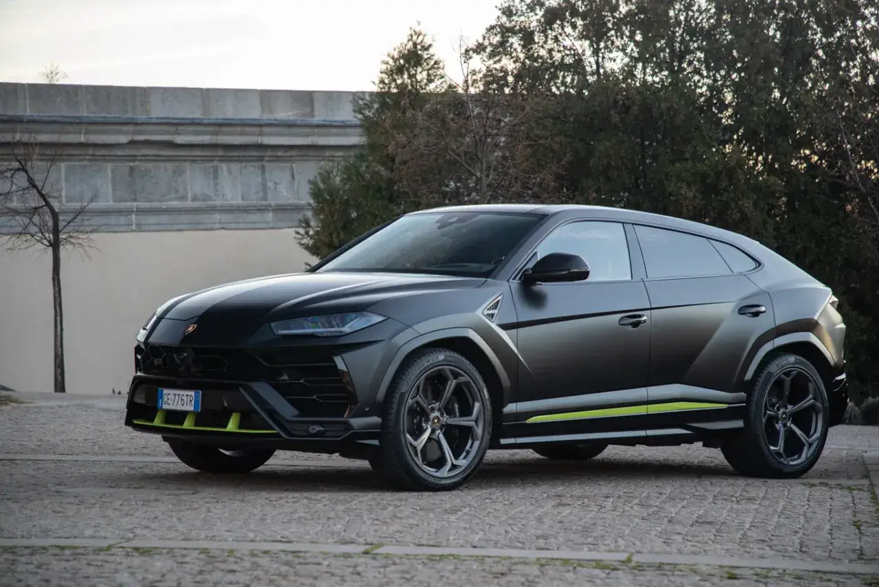 Un imponente **lamborghini urus negro** se exhibe con detalles en verde lima, destacando su diseño agresivo y deportivo sobre un fondo de piedra y vegetación.