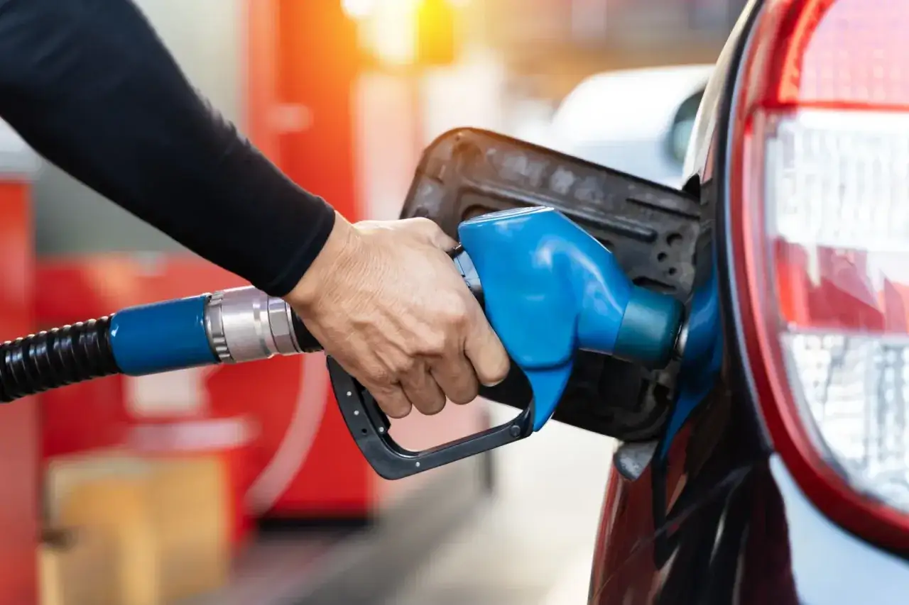 Dłoń trzymająca niebieski pistolet paliwowy, pokazująca, jak zatankować auto. Tankowanie samochodu na stacji benzynowej.