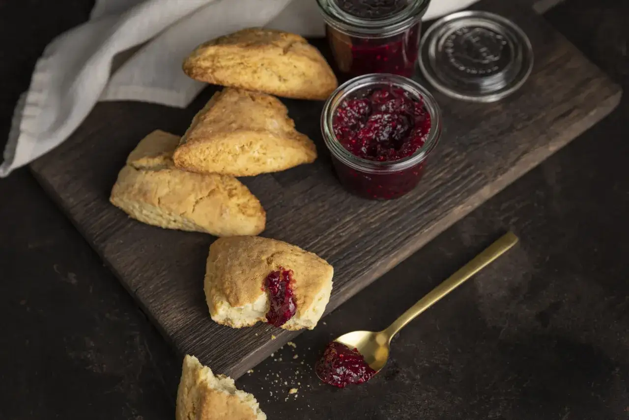 Goldene Scones mit Himbeermarmelade auf einem Holzbrett. Was sind Scones? Diese leckeren Gebäcke sind perfekt zum Tee.