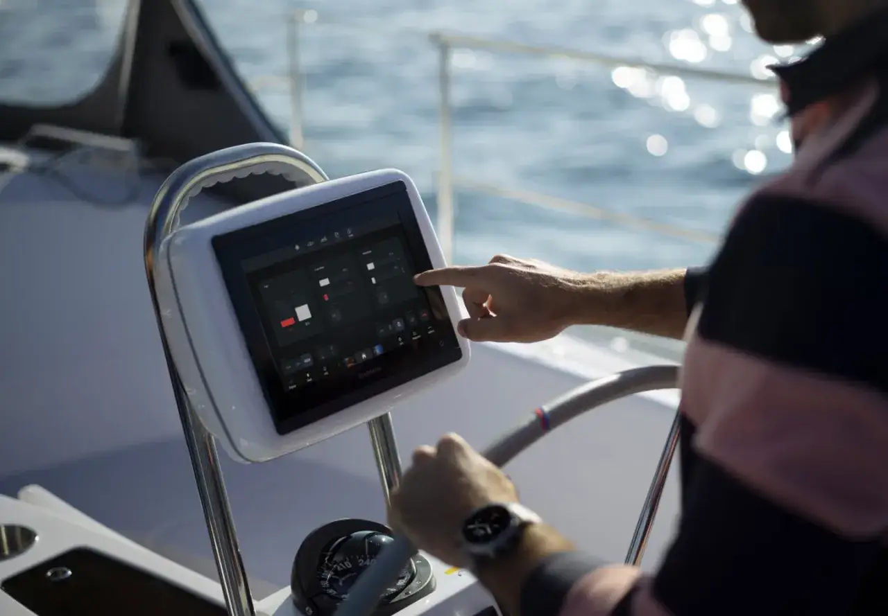 Un homme utilise un &eacute;cran tactile pour surveiller son bateau &agrave; distance, naviguant sur les eaux bleues.