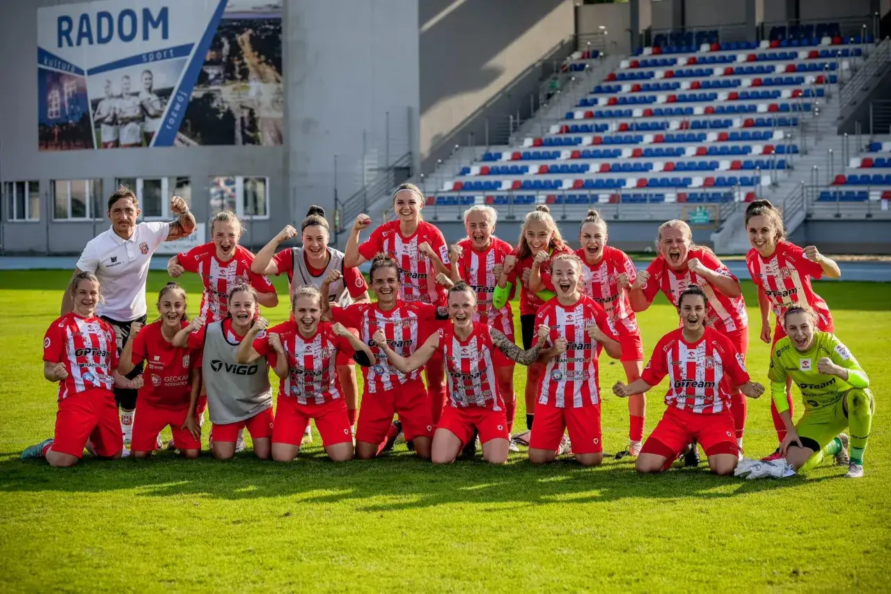 Radosny skład Resovii świętuje zwycięstwo na boisku. Piłkarki w czerwono-białych strojach pozują do zdjęcia z trenerem.