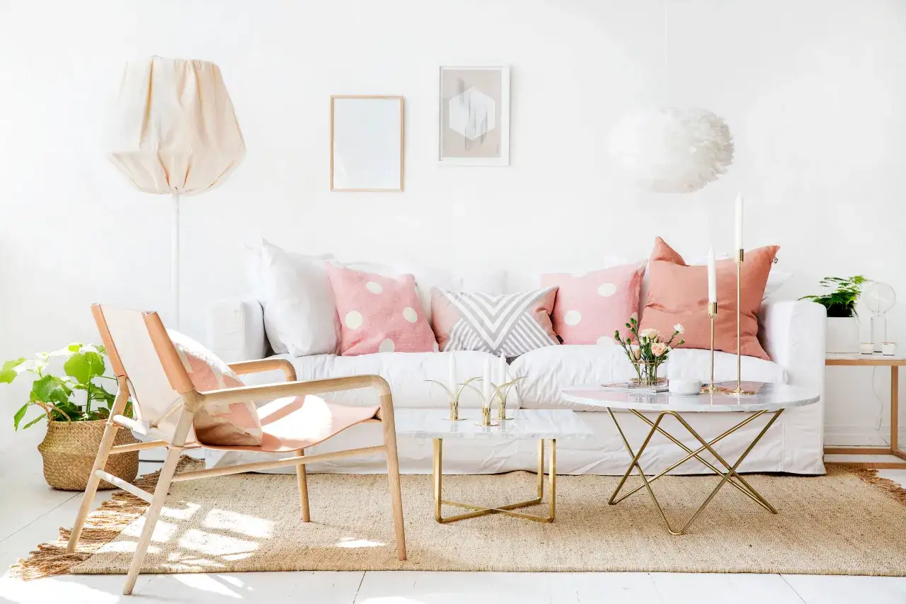 Gemütliches Wohnzimmer im hygge stil mit weißem Sofa, Korbstuhl, Marmortischen und Deko-Kissen in Rosa und Grau.