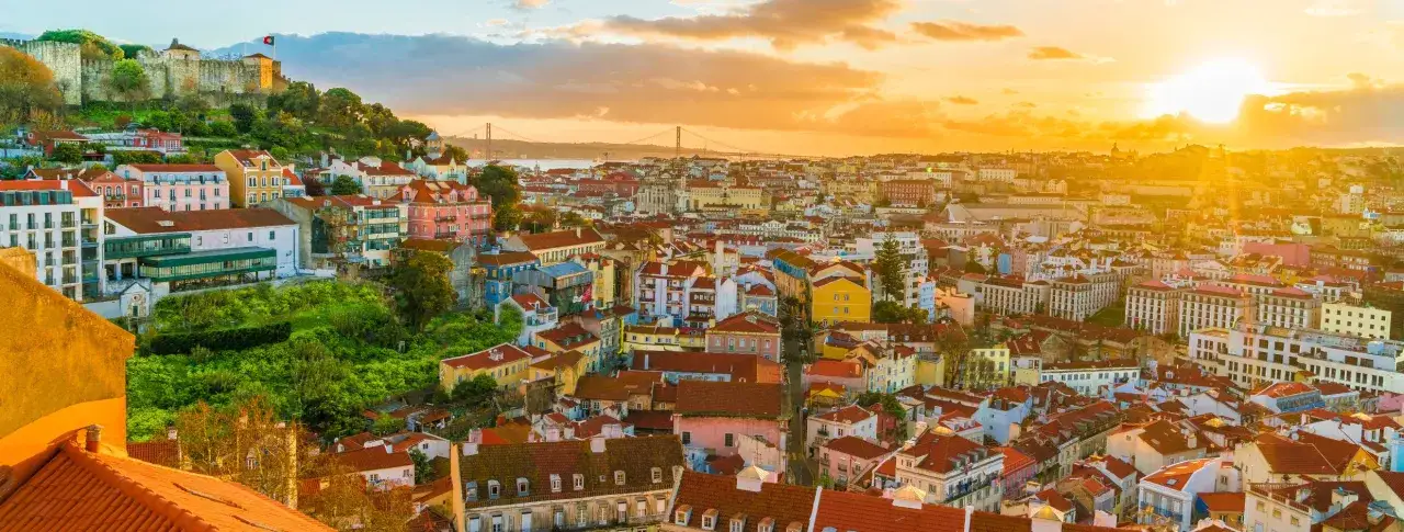 Bunte Häuser und eine Burg prägen das Bild der Hauptstadt Portugals bei Sonnenuntergang.