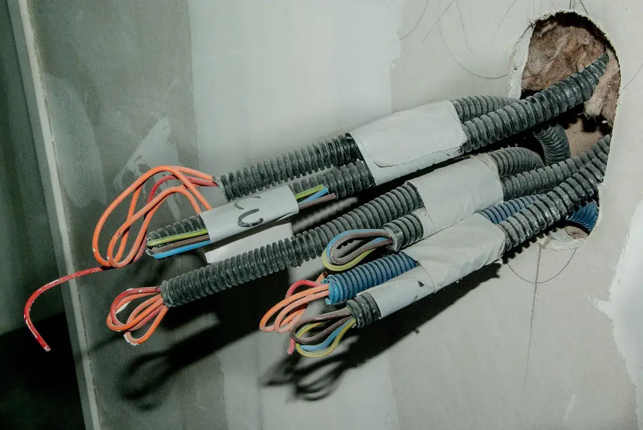 Instalacja elektryczna w trakcie prac: łączenie kabli w ścianie bez puszki, widoczne peszle i kolorowe przewody wychodzące z otworu.