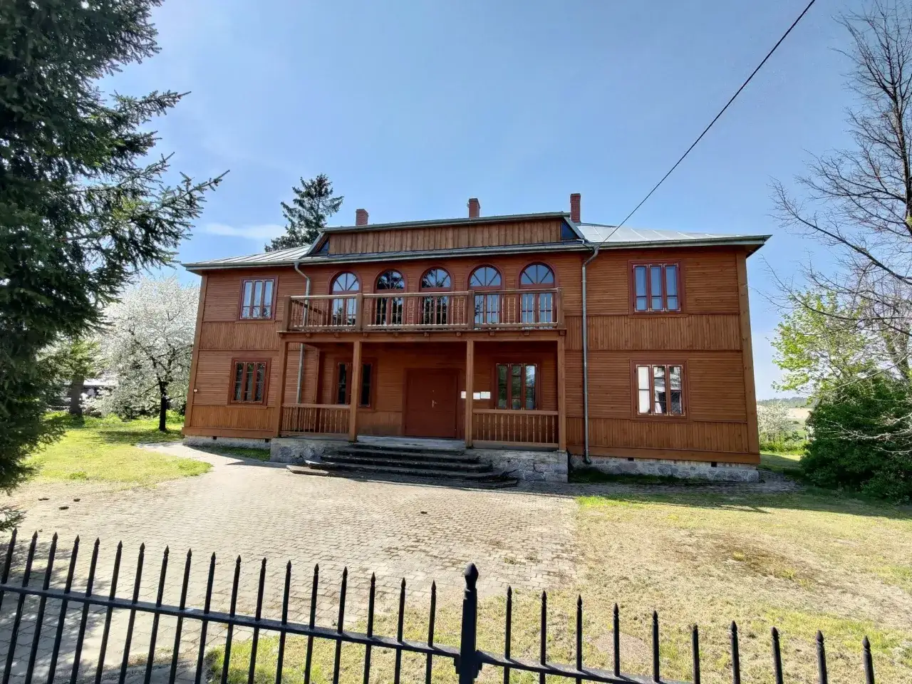 Drewniany dom z werandą i łukowymi oknami, otoczony zielenią. To jedna z urokliwych atrakcji w Zambrów.