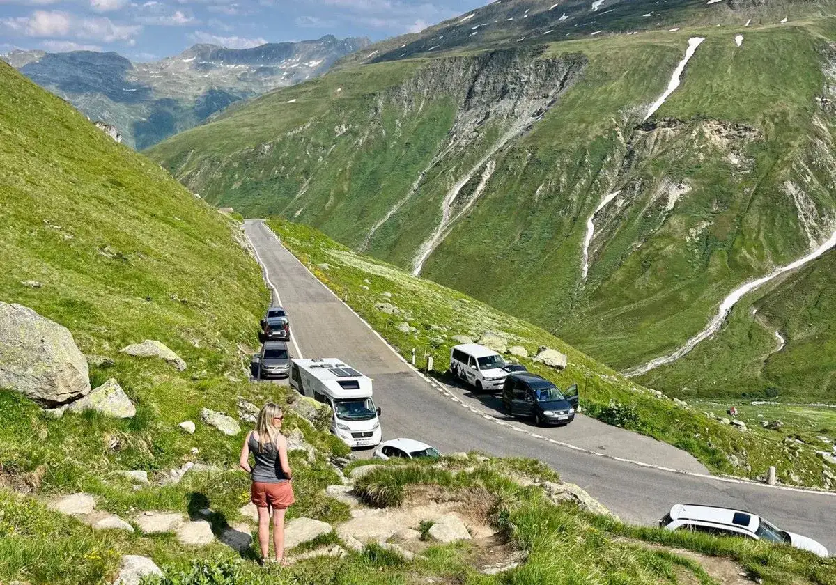 Une femme admire le paysage alpin, avec une route sinueuse bordée de camping-cars en Suisse.