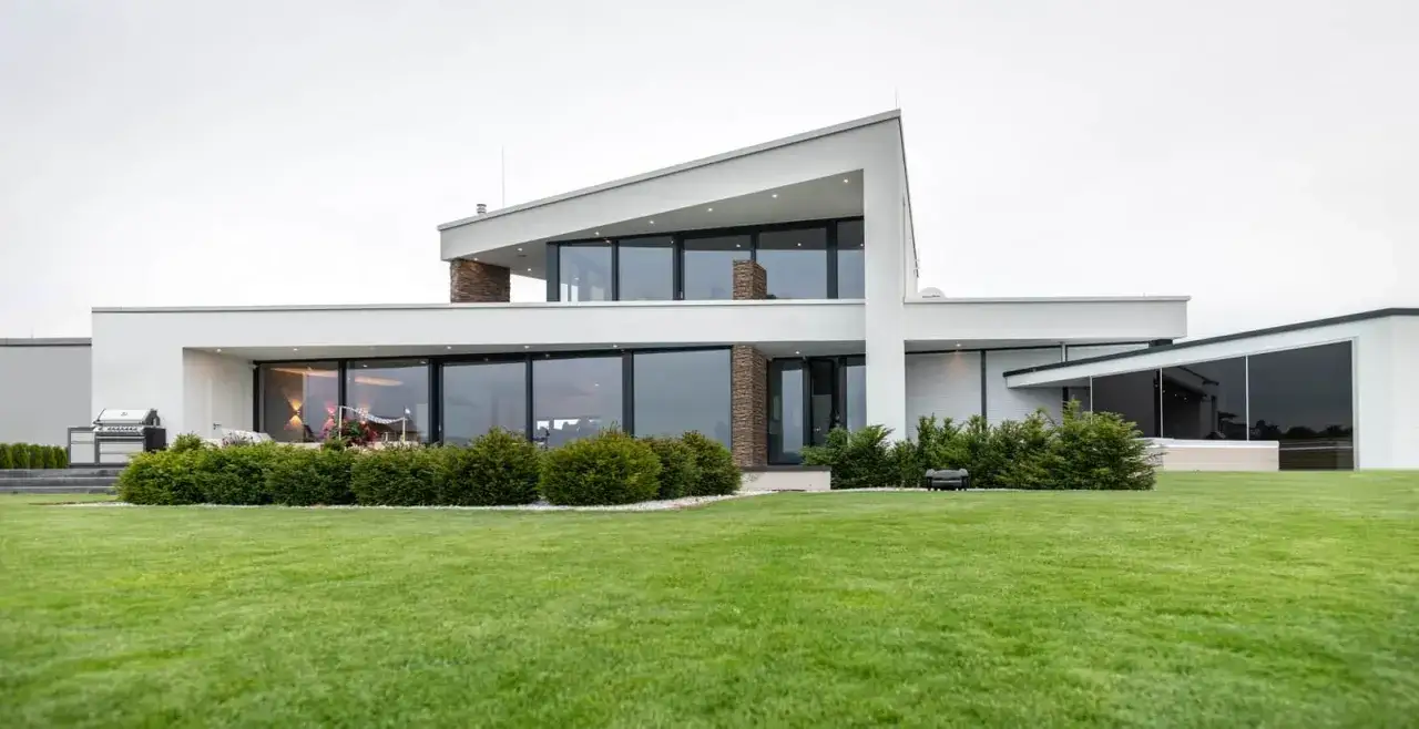 Modernes Einfamilienhaus mit dachterrasse, großen Glasflächen und gepflegtem Rasen.