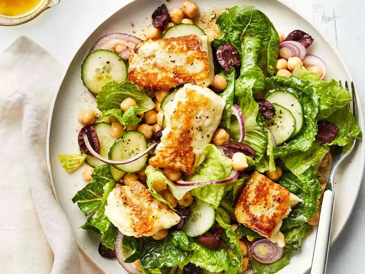 Szybki obiad na piątek bezmięsny: sałatka z chrupiącą sałatą, ciecierzycą, ogórkiem, oliwkami i grillowanym serem halloumi.