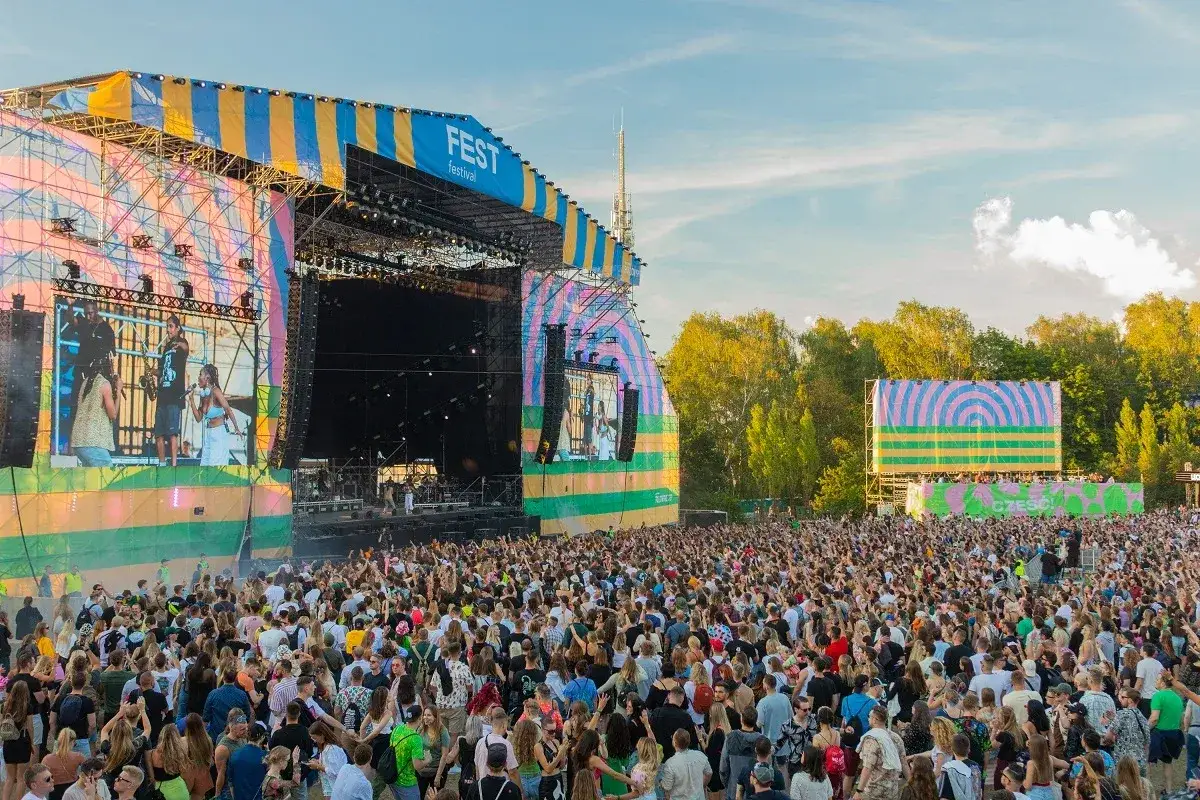 Tłum ludzi na fest festiwal pod wielką sceną. Słońce świeci, a niebo jest błękitne.