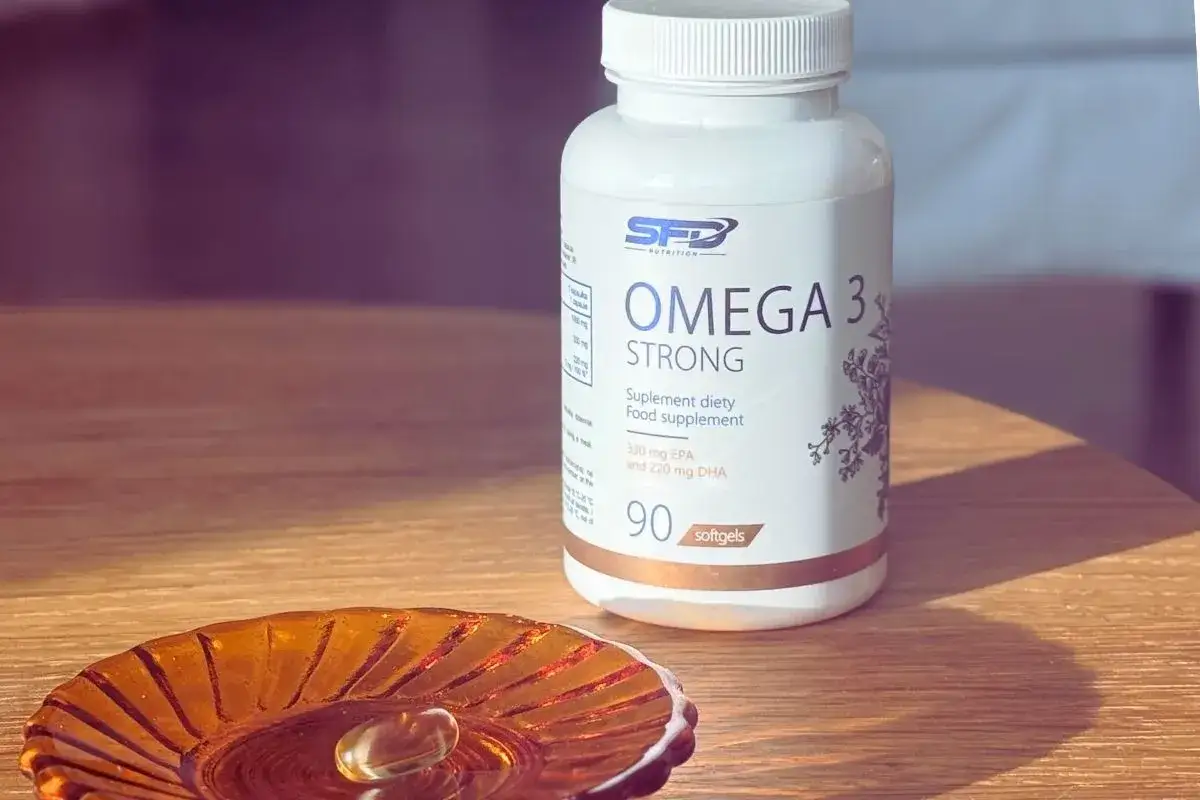 Butelka suplementu diety Omega 3 Strong i jedna kapsułka na ozdobnej podstawce.