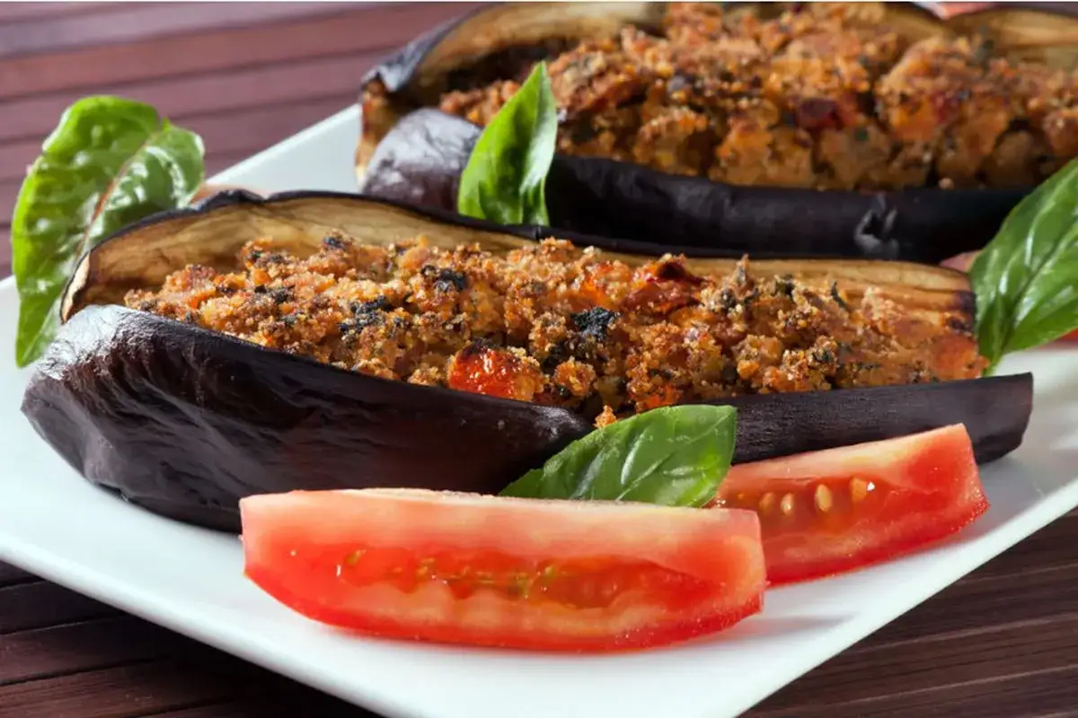 Melanzane a barchetta ripiene, guarnite con basilico fresco e fette di pomodoro, un piatto invitante.