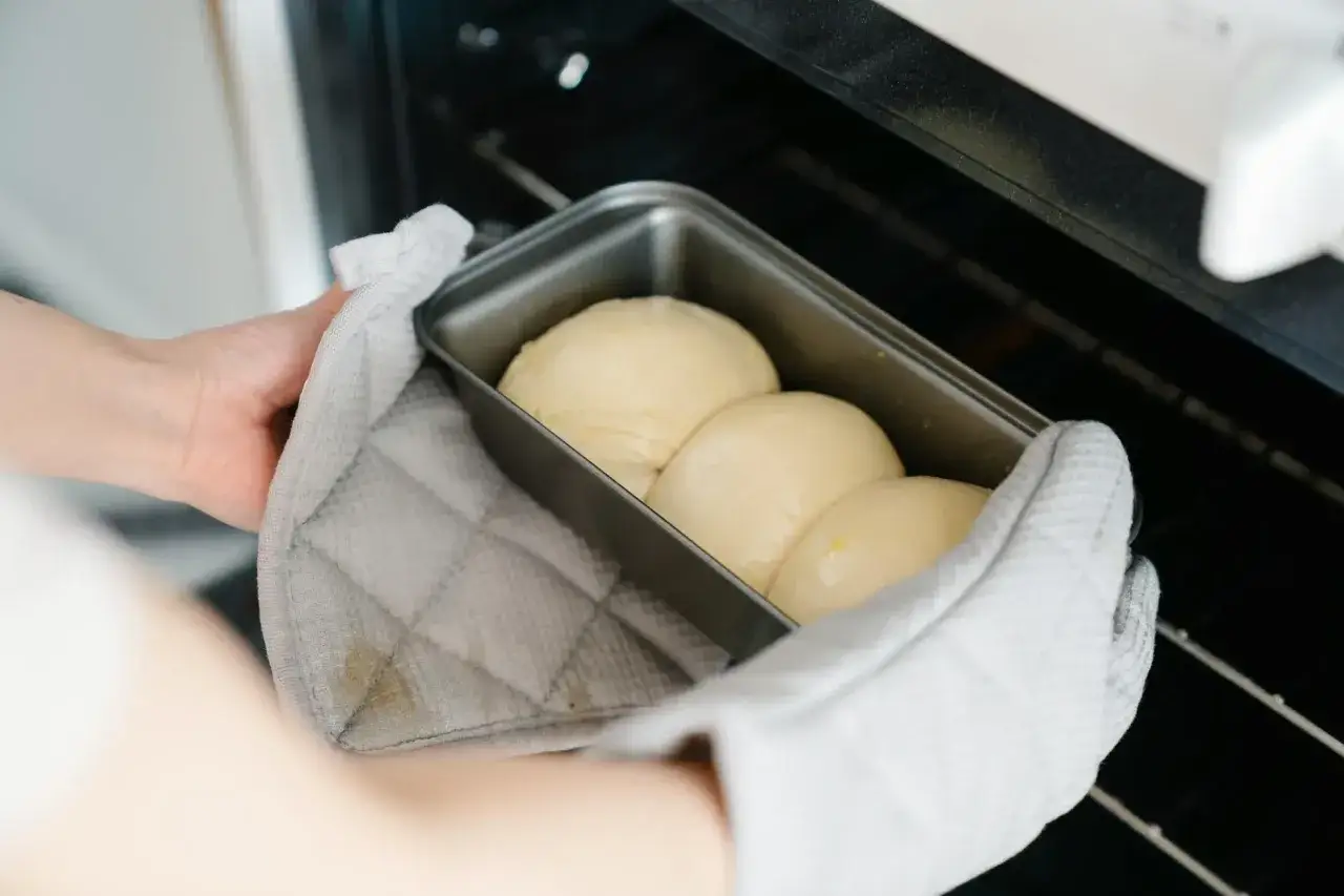 Ręce w rękawicy kuchennej wkładają formę z ciastem do piekarnika. Idealna temperatura pieczenia bezy zapewni chrupkość.