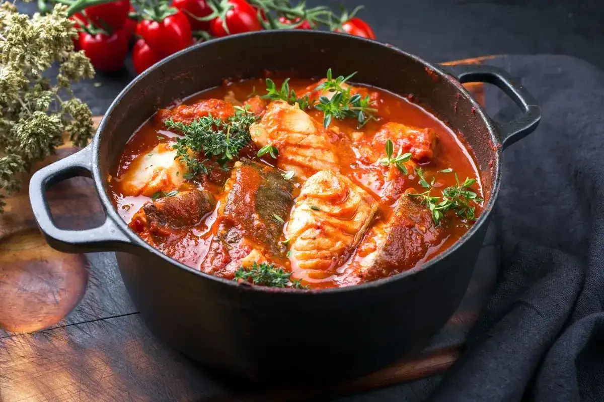 Un saporito cacciucco alla livornese in una pentola di ghisa, con pomodori freschi e erbe aromatiche sullo sfondo.