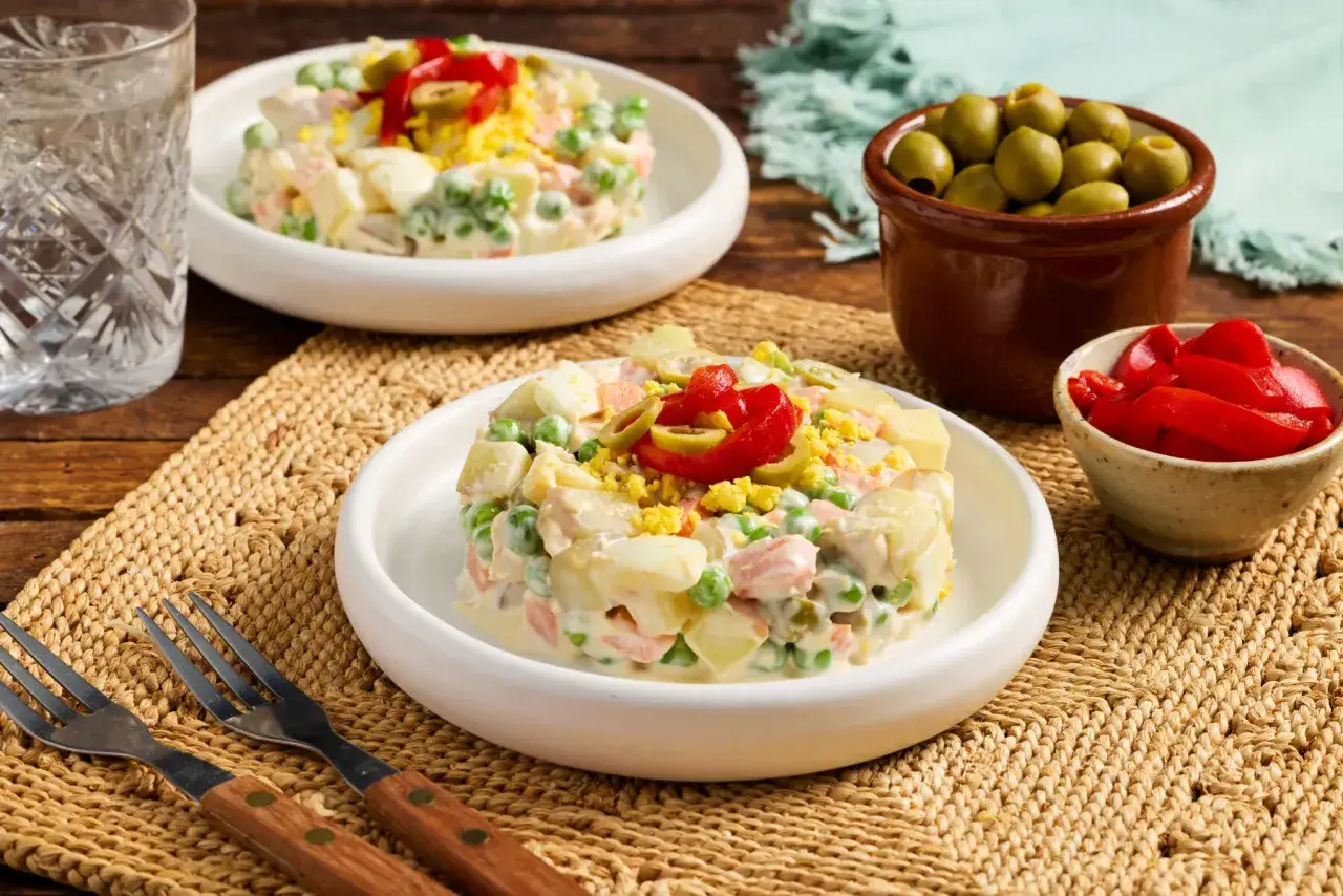 Two servings of ensalada rusa española, a creamy potato salad with peas, carrots, and egg, garnished with olives and red pepper.