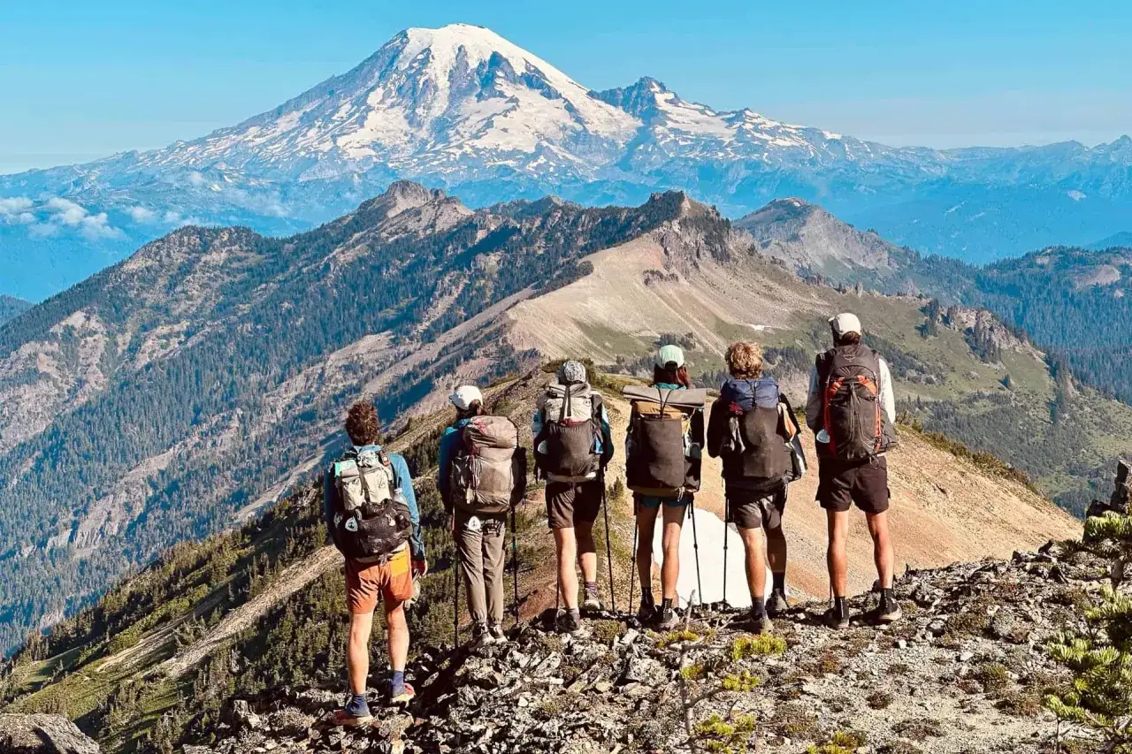 Grupa turystów na grani, podziwiająca majestatyczny ośnieżony szczyt. Widok zapiera dech w piersiach, jakby byli na szlaku Pacific Crest Trail.