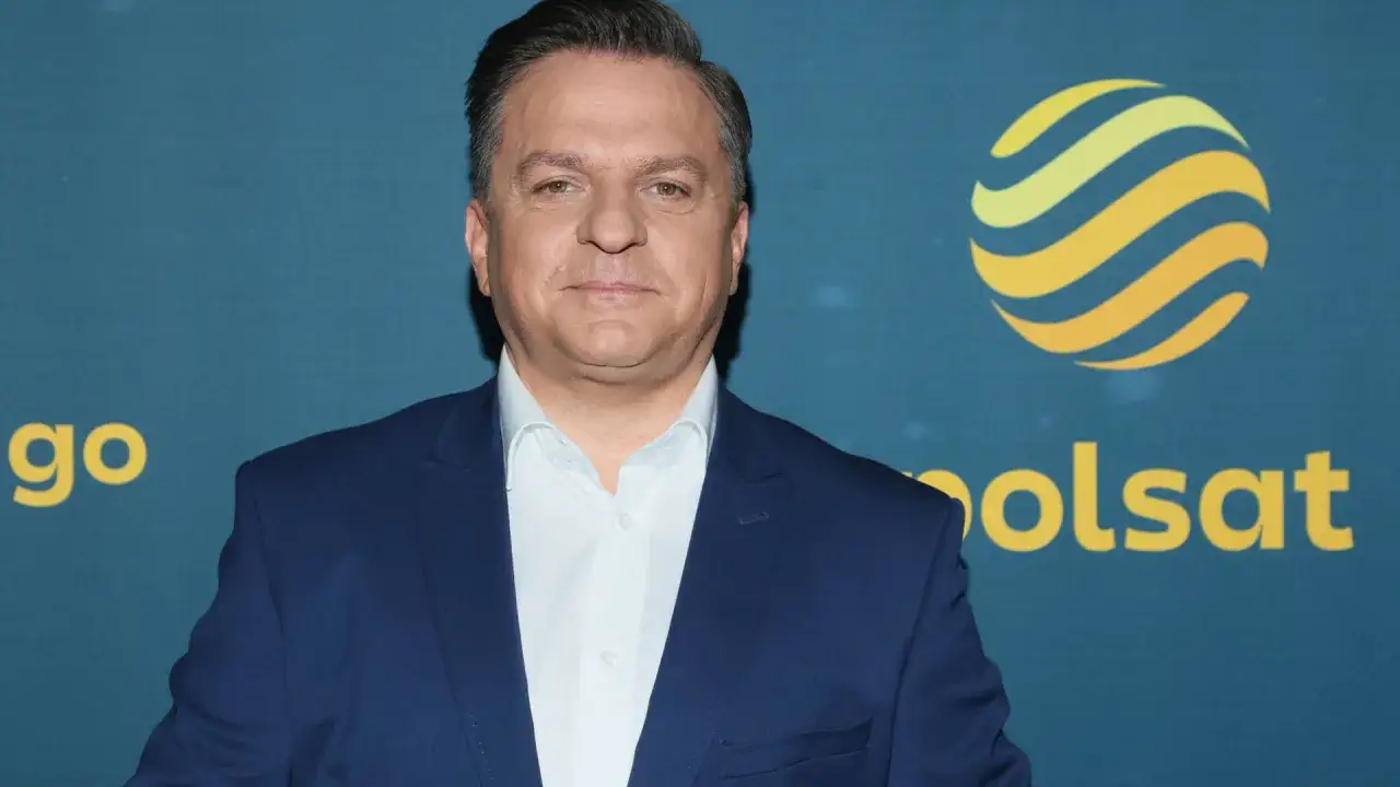 Rymanowski, znany z Polsatu, pozuje przed logo stacji.