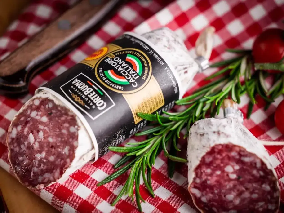 Zwei italienische Salsiccia-W&uuml;rste, die auf rot-wei&szlig; kariertem Tuch liegen. Die korrekte Salsiccia Aussprache ist wichtig f&uuml;r den Genuss.