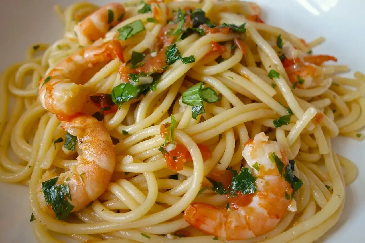 Un plat app&eacute;tissant de spaghetti aux crevettes, garni de persil frais et de morceaux de tomates.