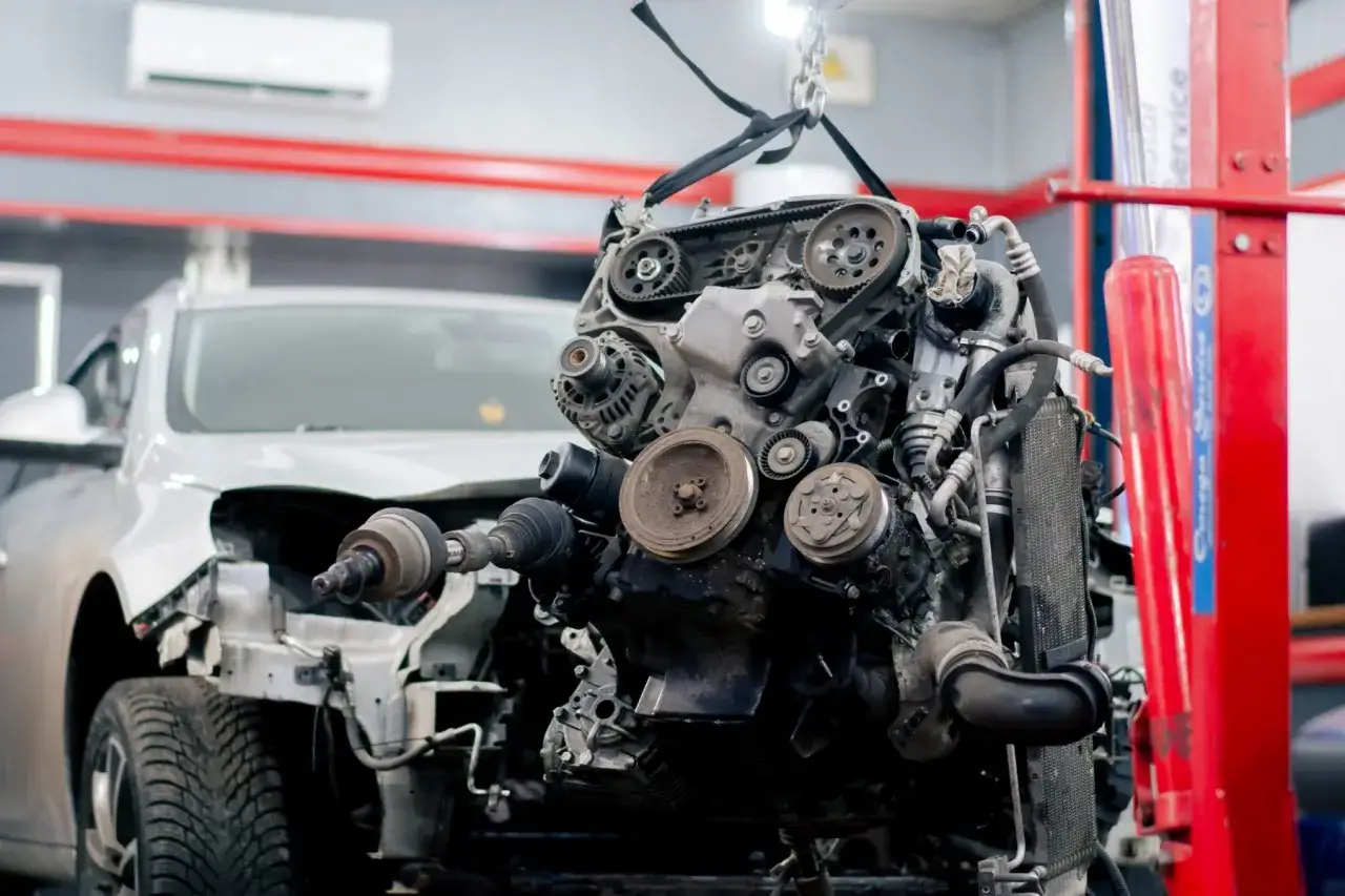 Silnik samochodowy zawieszony na haku, gotowy do naprawy. Czy AC obejmuje uszkodzenie silnika? Mechanik ocenia stan techniczny.