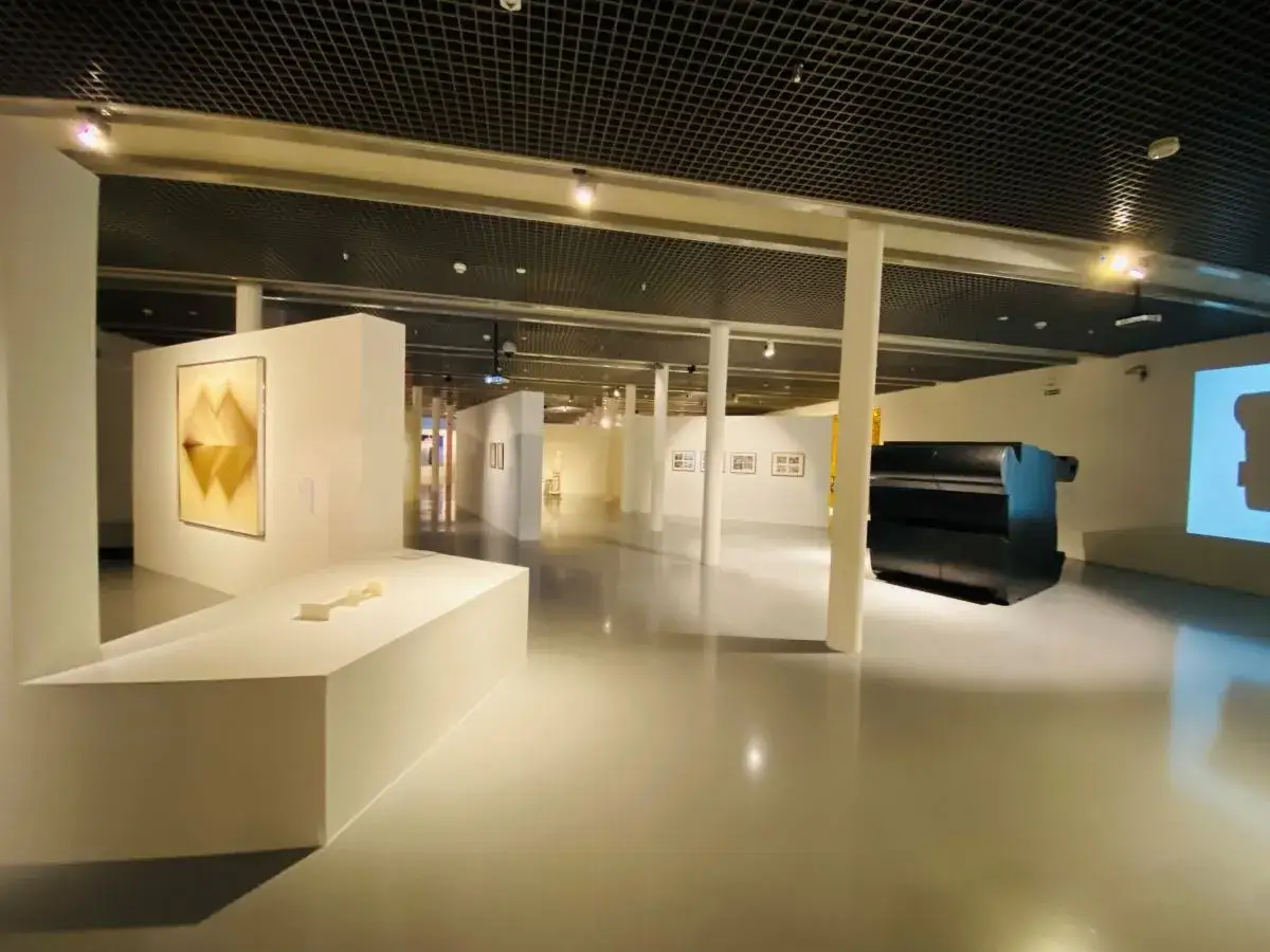 Wnętrze muzeum sztuki współczesnej w Łodzi. Widać abstrakcyjną rzeźbę, obrazy i projekcję wideo.