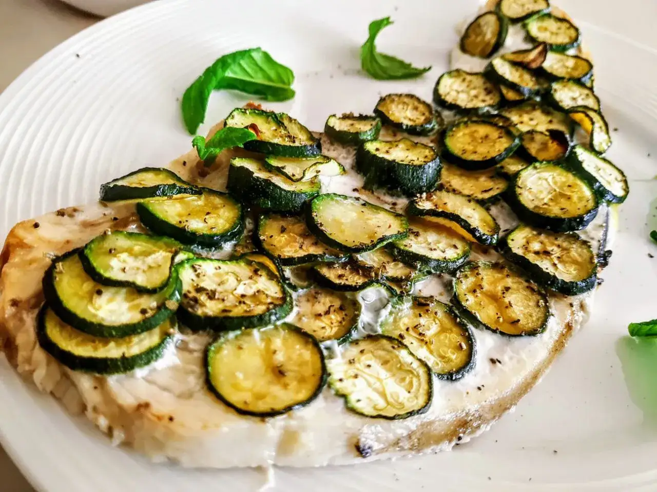 Delizioso pesce spada al forno con zucchine grigliate e una crema leggera, guarnito con basilico fresco.